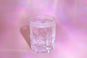 A glass of water on a pink background.