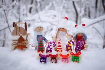 Toy angels in knitted hats and scarves. There are dwarfs and gifts nearby. Christmas decorations. Snow background.