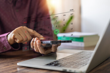 Businessman using smartphone and laptop to plan A green checkmark on the 15th January 2026 calendar. Concept of digital schedule, mobile banking, time management, remote work, online appointment.