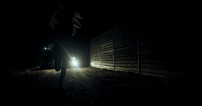 Girl runs in the dark from police lights behind a wooden fence on a deserted path during the night