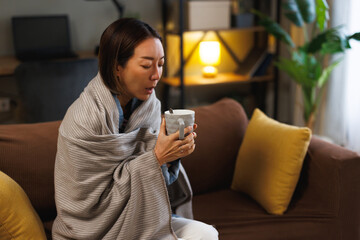 Sick Asian woman coughing while holding mug on couch