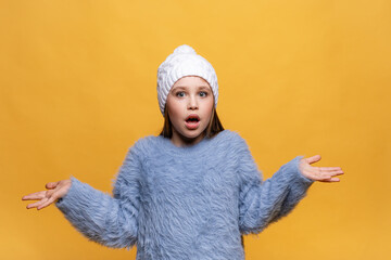 Puzzled and clueless little girl with arms out, shrugging her shoulders, on yellow background, saying: who cares, so what, I don't know. Negative human emotions, facial expressions, life attitude