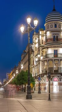 Avenida de la Constitucion day to night timelapse in Seville, Spain. Iconic Adriatica building glowing after sunset. Historic architecture with modern streetlights, pedestrians and urban atmosphere