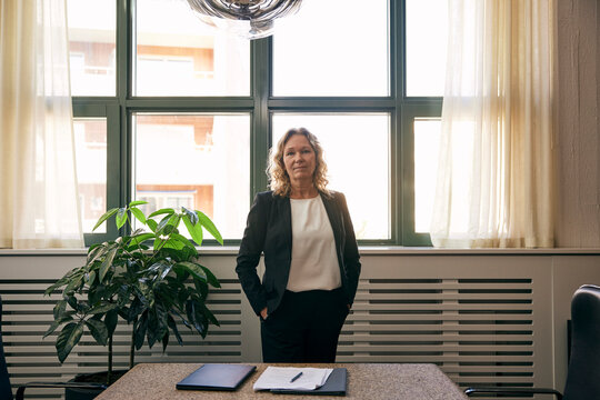 Portrait of confident female lawyer standing with hands in pockets at office