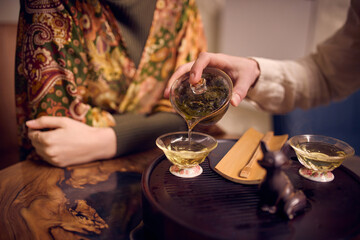 Man pouring hot tea into glass cup during traditional tea ritual. Concept of mindful preparation, tea culture practices, calm domestic moments, slow living aesthetics and lifestyle storytelling.