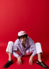 Stylish young man poses creatively against vibrant red backdrop during an artistic photoshoot