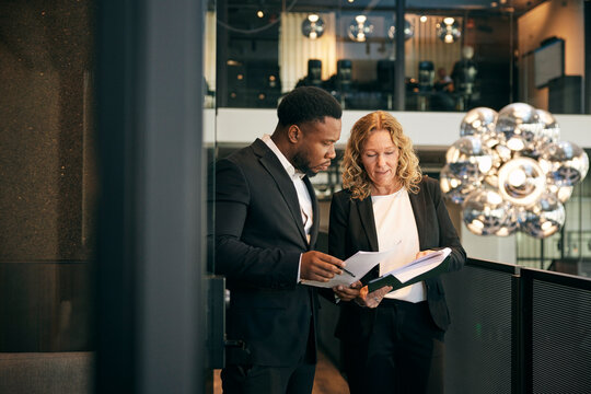 Male and female business experts discussing documents with each other in corridor at law firm