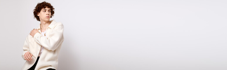 Young stylish man poses effortlessly in modern attire against a clean backdrop