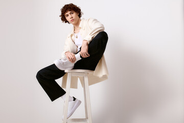 Stylish young man exudes confidence in trendy outfit while posing on a stool indoors
