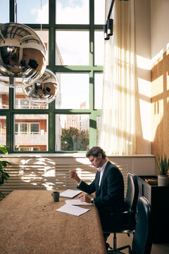 Concentrated male business professional examining agreement papers while sitting at table in law firm
