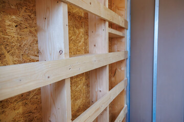 Close up interior wall framing shows planed softwood studs and noggins against OSB, with a metal...
