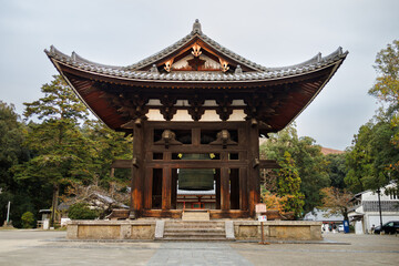 Ancient Japanese Temple Gate With Large Bell And Curved Roof In Serene Garden Setting. Nara City, Japan