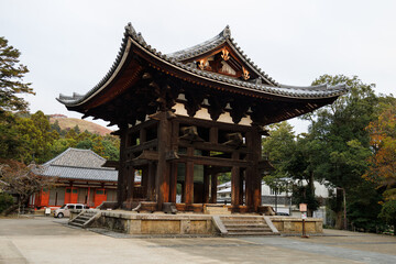 Fototapeta premium Ancient Japanese Temple Gate With Large Bell And Curved Roof In Serene Garden Setting. Nara City, Japan