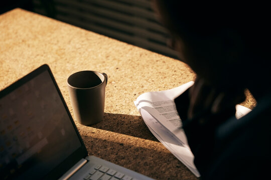 High angle view of sunlight shining on coffee mug kept on table near paper and laptop