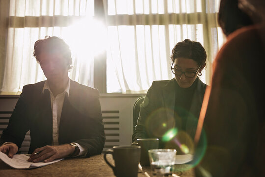 Sunlight shining through window of board room with male and female lawyers examining agreement papers