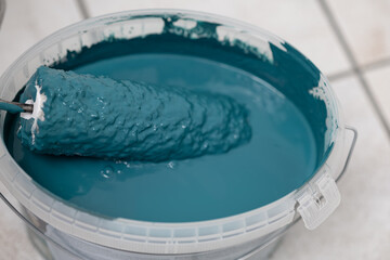 Paint roller immersed in teal paint inside a clear bucket, showcasing texture and color depth, ideal for home improvement and artistic projects with copy space