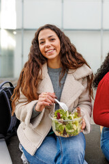 Smiling female student eating salad outdoors on college campus, focusing on wellness