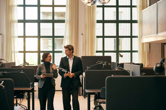 Male and female business professionals talking with each other while walking between office desks