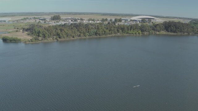 Aerial view of a vast lake adjacent to lush trees and the Carrasco International Airport, showcasing the tranquil waters, Ciudad de la Costa, Departamento de Canelones, Uruguay.