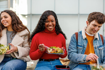 Three diverse friends eating salads and smiling during campus break