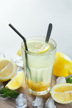 A tall glass of chilled lemon honey drink with lemon slice and honey sediment at the bottom, served with straw and spoon.