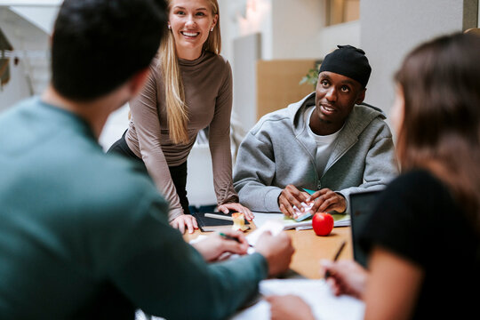 Smiling male and female student listening to friend sharing ideas during group discussion at college campus