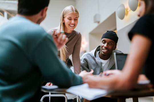 Smiling female student sharing ideas with friends during project discussion in university campus