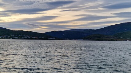 A fjord in Fauske, Norway, framed by rugged mountains and calm waters, is particularly striking in autumn. The surrounding slopes are painted in shades of gold, red, and orange as the deciduous trees 