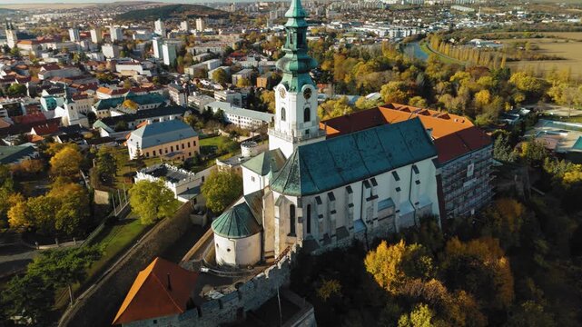 Aerial view of the grand Nitra Castle standing tall with its white walls and red roof, surrounded by trees in their autumn colors, Nitra, Nitra Region, Slovakia.