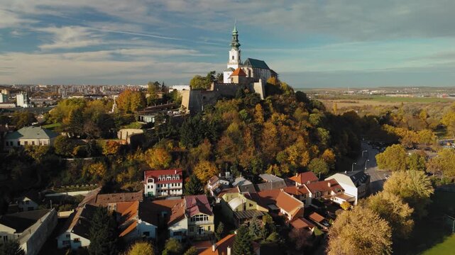 Aerial view of the majestic Nitra Castle perched atop a hill surrounded by autumn foliage, creating a vibrant contrast of colors, Nitra, Nitra Region, Slovakia.