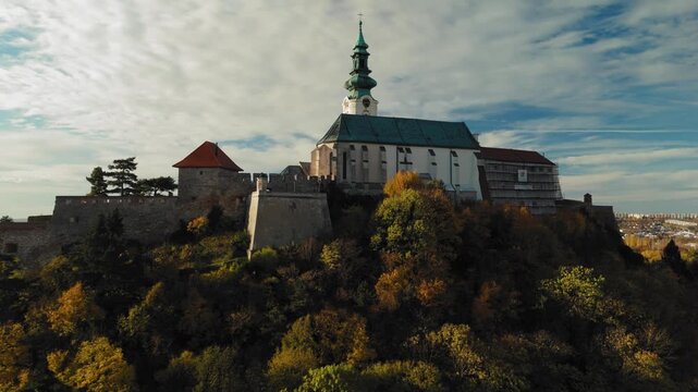 Aerial view of Nitra Castle atop a hill, showcasing its walls, towers, and church against a backdrop of autumn foliage, Nitra, Nitra Region, Slovakia.