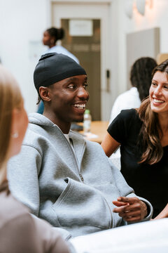 Smiling young man wearing do rag sitting with friends in college campus