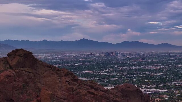 Aerial view of Phoenix city skyline with red rock formations and distant mountains under a cloudy sky, Phoenix, Arizona, United States.