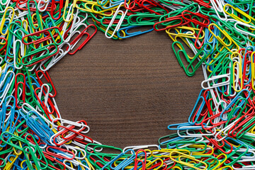 Top down photo of multicolored paper clips on the wooden table. Many paperclips on the table with copy space in the centre.