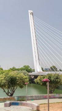 Alamillo Bridge with a tall pylon and steel cables spans over the Guadalquivir River in Seville, Spain. Timelapse hyperlapse of modern suspension design with busy traffic under a clear blue sky.