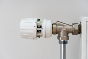 Close up view of thermostat of heating radiator with over white wall with copy space. Concept of heating season, setting a comfortable temperature at home and resources consumption.