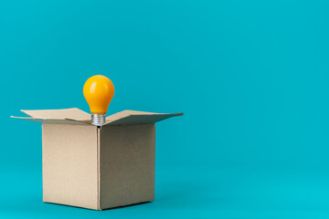 Opened recyclable cardboard box with yellow bulb in it over turquoise blue background. Thinking outside the box, great idea and creative problem solving concept with copy space.