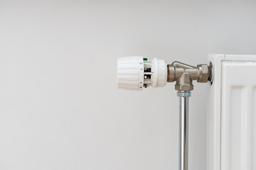 Close up view of modern heating radiator with thermostat in living room over white wall with copy space. Concept of heating season, setting a comfortable temperature at home and resources consumption.