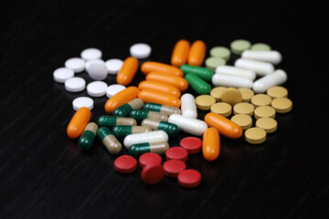 Pills and capsules scattered on a black wooden table. Background for pharmacy, antibiotics, vitamins, dietary supplements