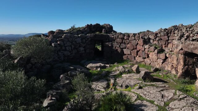 Aerial view of the weathered Nuraghe Burghidu stone ruins, a testament to ancient civilization against a backdrop of clear blue skies, Olmedo, Sardinia, Italy.