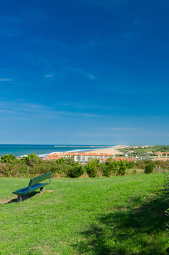 View of a lone green bench overlooking the endless blue sea and golden sandy beach under a clear sky, Anglet, France.