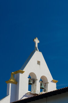 View of a crisp white church steeple topped with a cross and twin bells against a bold blue sky, a serene architectural moment, Anglet, France.