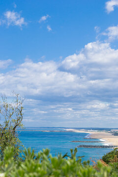 View of the tranquil turquoise sea meeting the sandy beach under a vast blue sky dotted with fluffy clouds, captured from a high angle, Anglet, France.