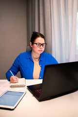 Student attending virtual university class via video conference. Young woman actively participates in online lecture, taking notes on laptop. Distance learning and educational technology concepts