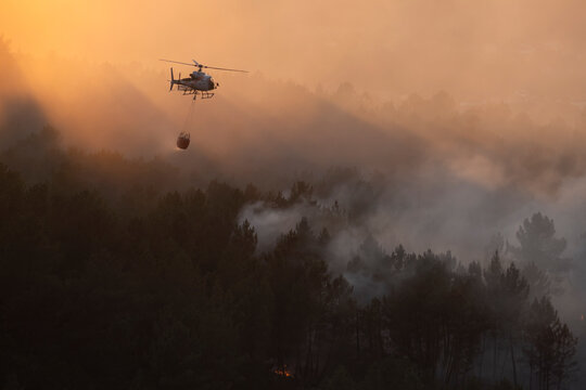 Water bomber helicopter with red helibucket working in the Ourense wildfires