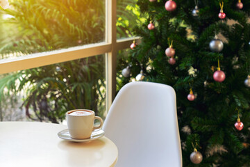 Embracing holiday spirit with delicious hot cappuccino on table near window and beautiful view of decorated Christmas tree in background. hot cup of coffee with Merry Christmas festive decorations.