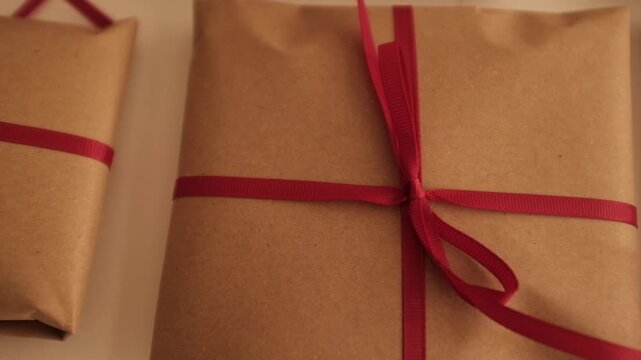 Christmas presents wrapped in brown craft paper and tied with thin red ribbon. Simple and modern wrapping aesthetics. Winter holidays gift giving tradition. Secret Santa.