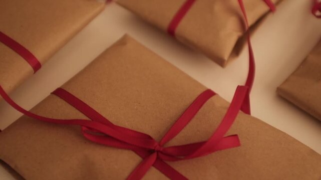 Christmas presents wrapped in brown craft paper and tied with thin red ribbon. Simple and modern wrapping aesthetics. Winter holidays gift giving tradition. Secret Santa.