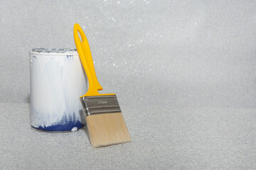 A can of white paint and a brush on a gray textured background. Copy space. Home or apartment renovation concept