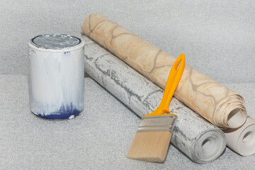 Textured wallpaper, a can of white paint, and a brush on a gray background. Space for text. Concept for a home or apartment renovation
